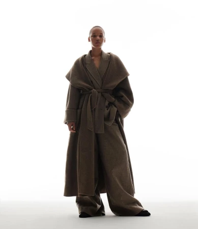 Model wearing a brown belted coat and matching wide trousers against a bright white background