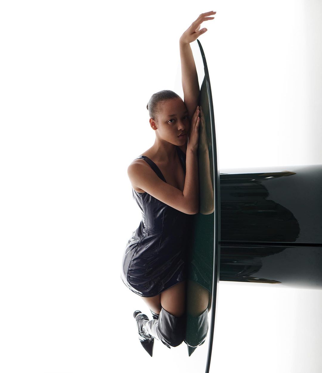 Attractive young woman in a dark mini dress and shiny boots poses with a black oval frame against a bright white background in a studio.