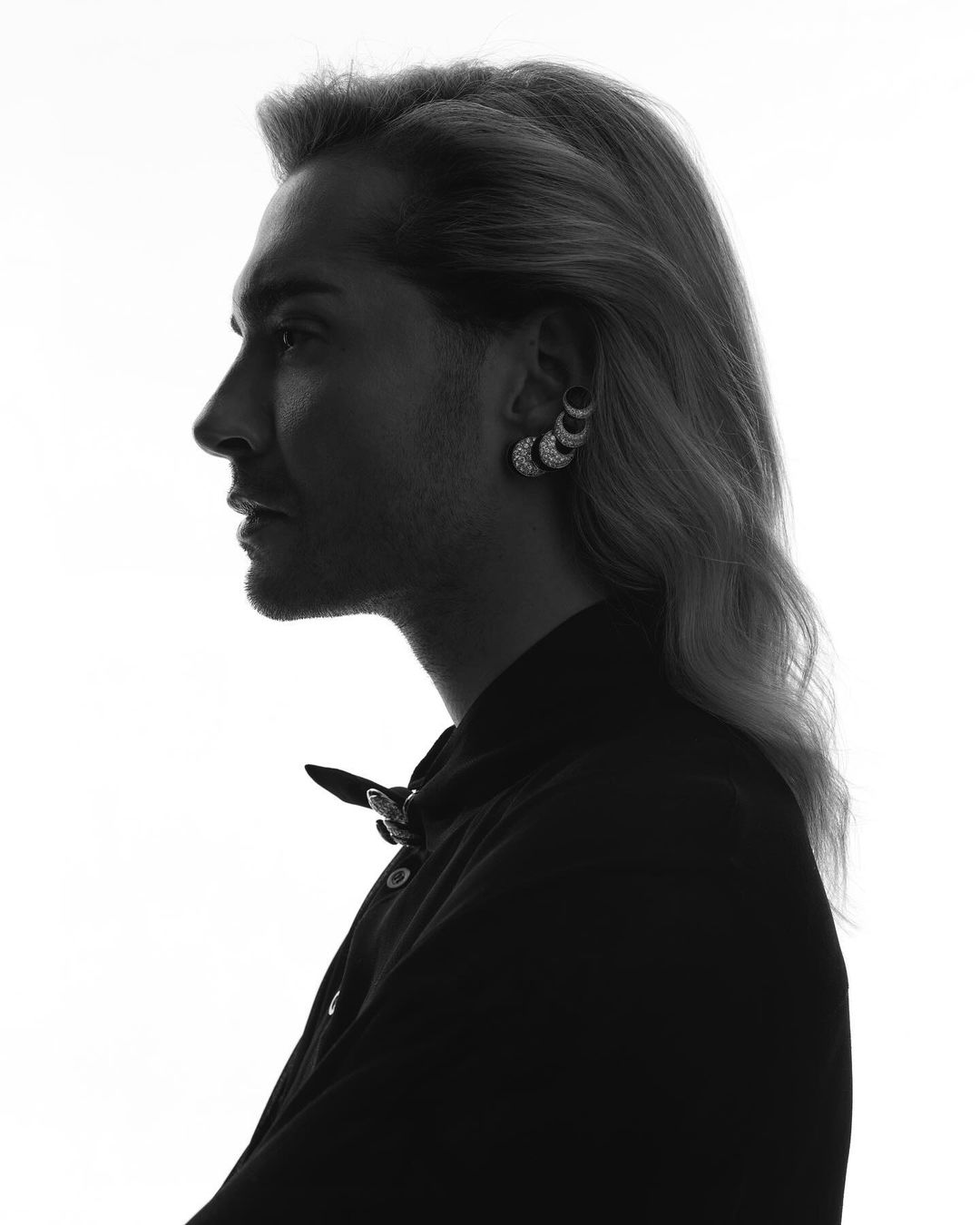 Profile portrait of a person with long hair wearing an ear cuff, silhouetted against a bright white background.