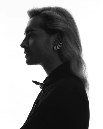Profile portrait of a person with long hair wearing an ear cuff, silhouetted against a bright white background.