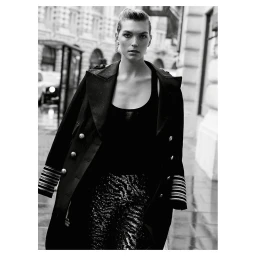 Black and white portrait of a woman wearing a dark double-breasted coat on a wet city street by Mel Karch.