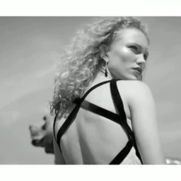 Monochrome portrait of a woman with curly blonde hair wearing a strappy dress, looking back over her shoulder outdoors