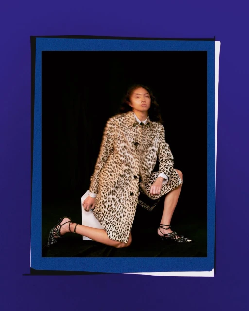 Woman in leopard-print coat poses in a blue-framed photo, creating a fashion editorial look with dark backdrop and stylish outfit.