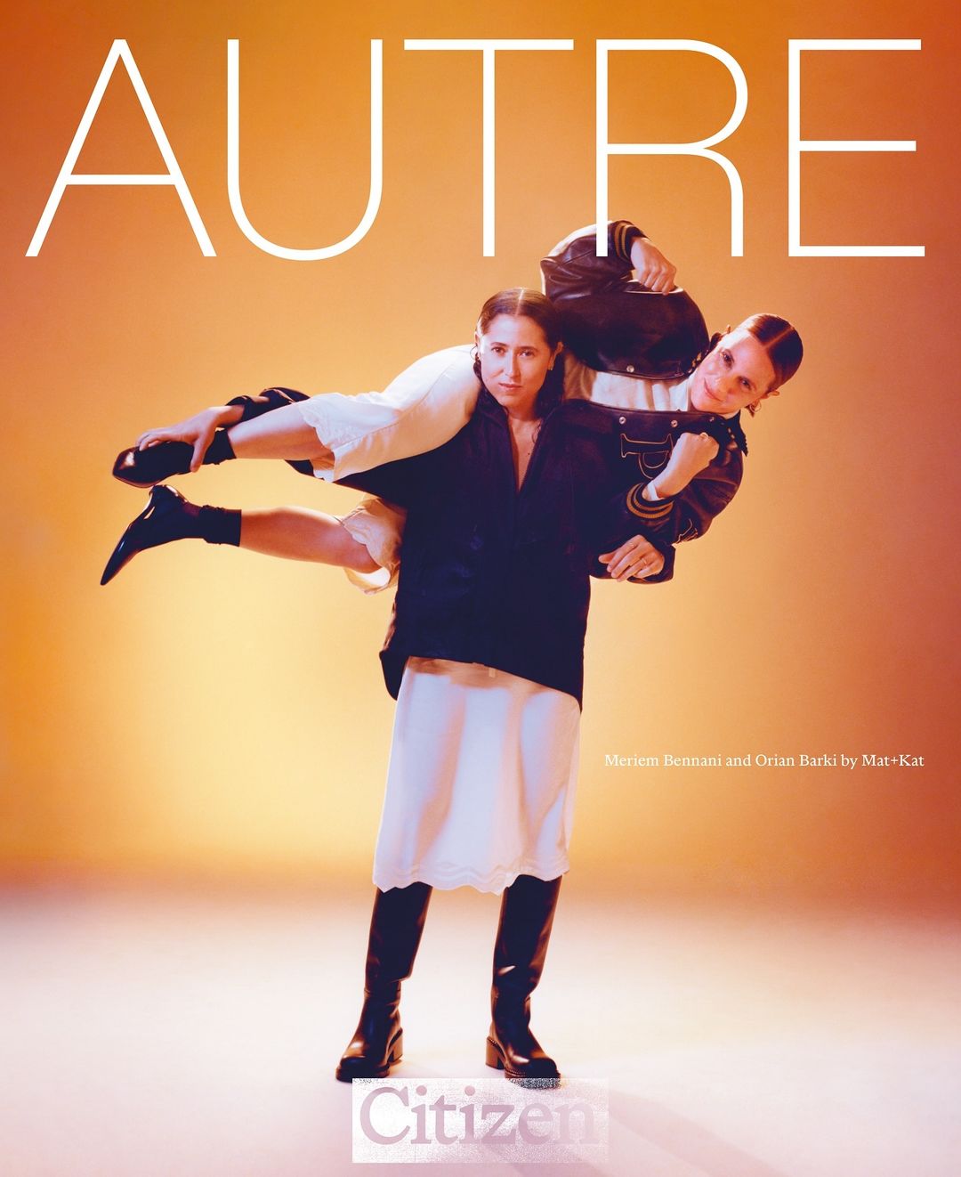 Two women in a playful pose, one carrying the other on her shoulders. Fashion shot with a gradient orange backdrop and editorial lighting.