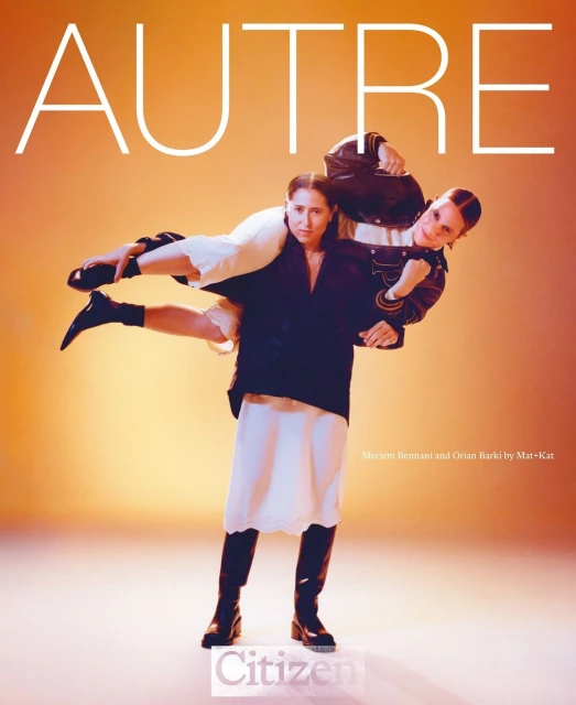 Two women in a playful pose, one carrying the other on her shoulders. Fashion shot with a gradient orange backdrop and editorial lighting.