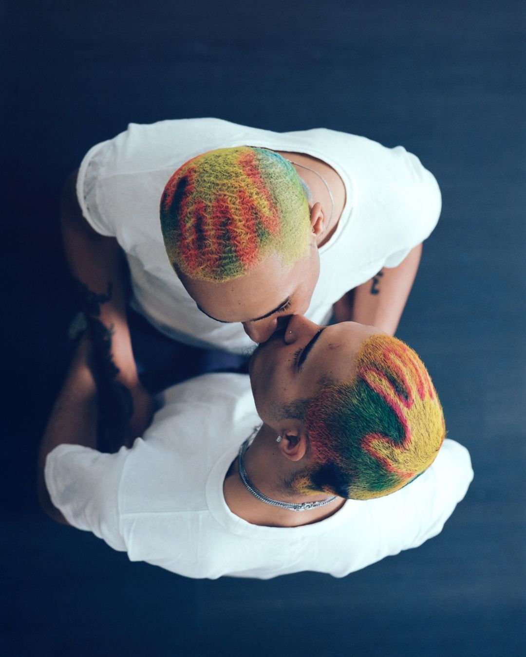 Overhead shot of a couple embracing, showcasing their vibrantly colored hair against a dark background, creating a striking visual contrast.