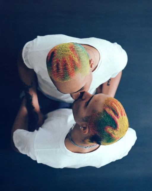 Overhead shot of a couple embracing, showcasing their vibrantly colored hair against a dark background, creating a striking visual contrast.