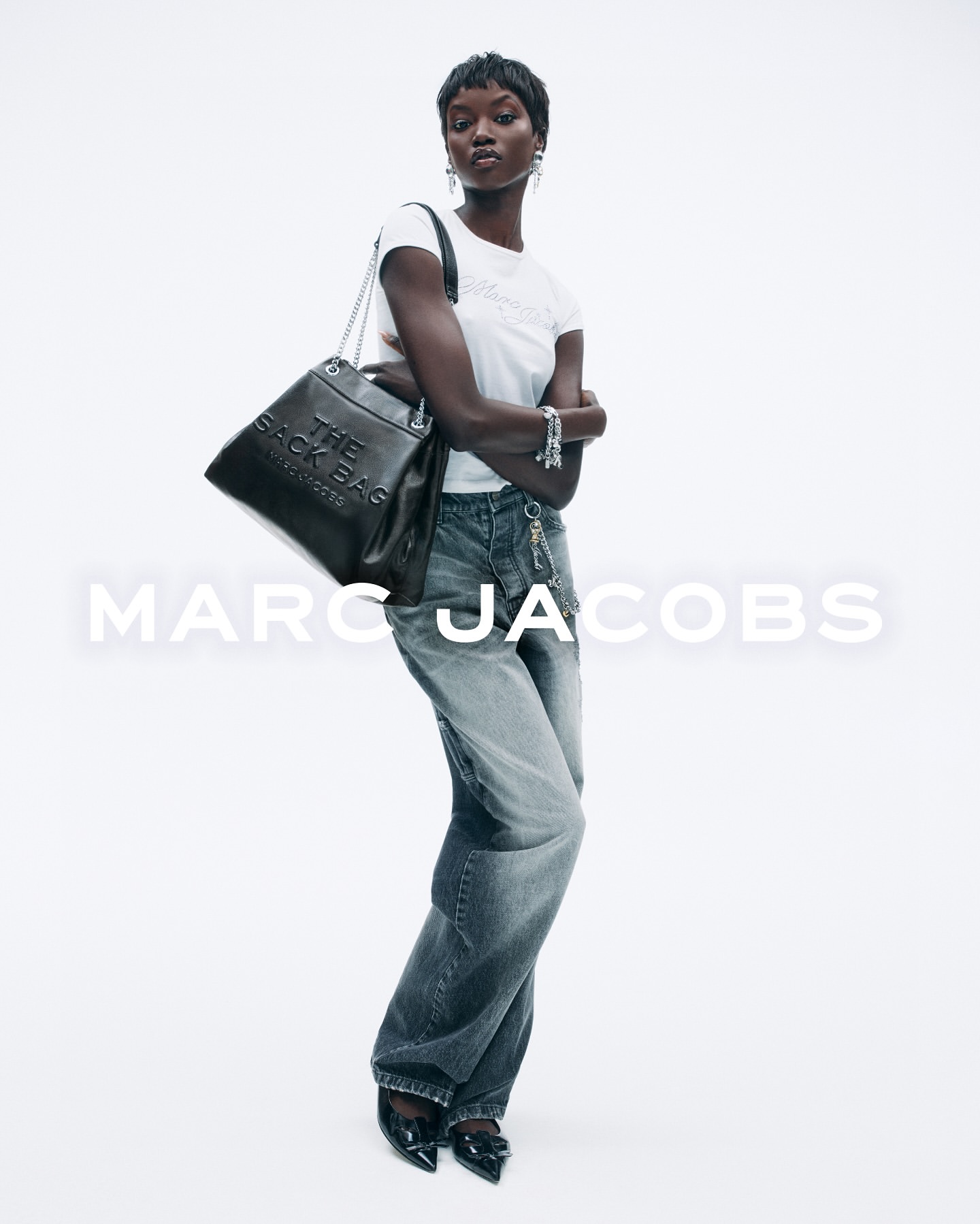 Model in white t-shirt and grey jeans wearing a black leather shoulder bag against a white background with text
