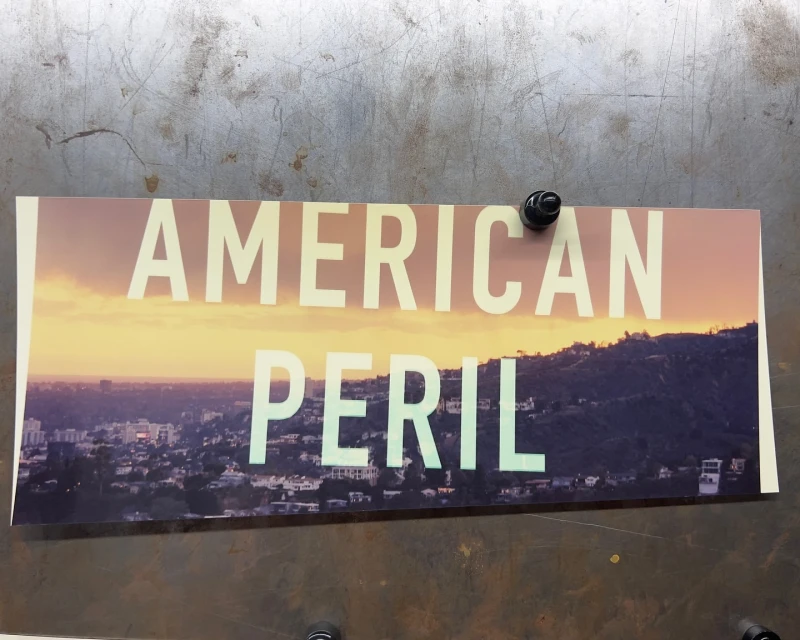 Poster featuring an urban landscape with the words 'American Peril' in bold white letters against a sunset sky.