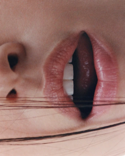 Close-up view of an adult female's face featuring her open mouth, teeth, and tongue with stringy hair, oriented vertically.
