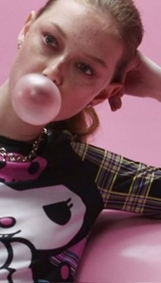Woman with pink bubblegum bubble posing in front of a pink background wearing a graphic shirt and silver chain.