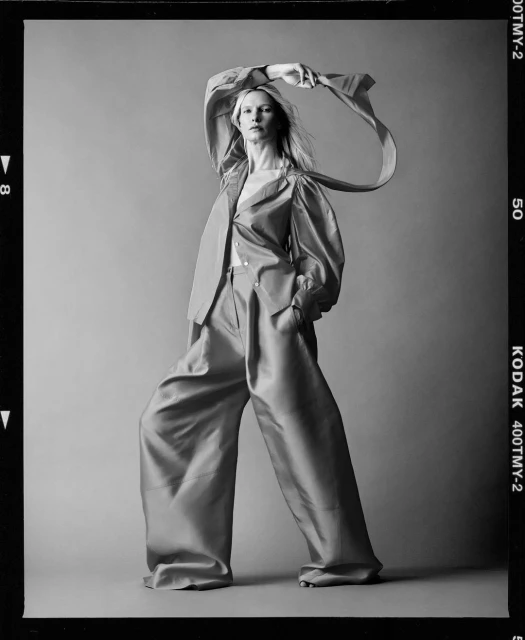 A woman with fair skin poses in a photo studio wearing a copper-colored pantsuit with long, wide-legged pants, and a matching jacket.