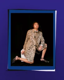 Model wearing a leopard print coat kneeling against a black backdrop framed by layered colored borders