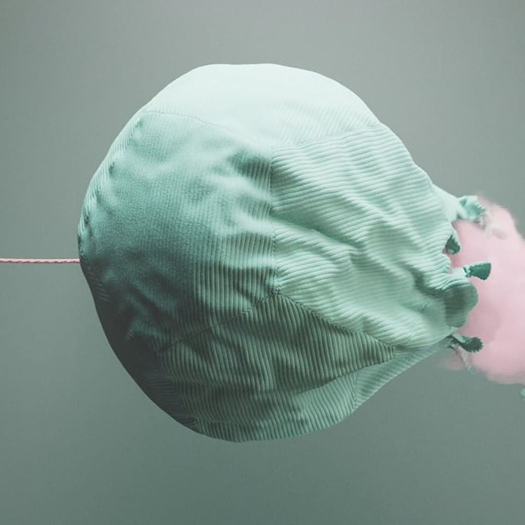 Soft light green fabric bag suspended in mid-air with a light pink puff of cotton candy behind it against a matching green backdrop.