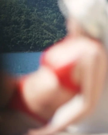 Woman in red bikini relaxes by the water with a backdrop of green mountains. Summer leisure and vacation in a blurred image.