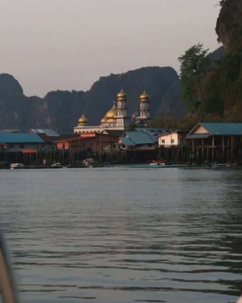 Coastal village with a mosque featuring golden domes, set against a backdrop of islands and a tranquil body of water.