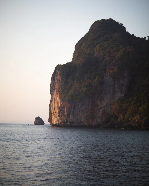 Large rock formation juts out from the ocean with smaller rock island in background under bright sky during daytime. Nature photography.