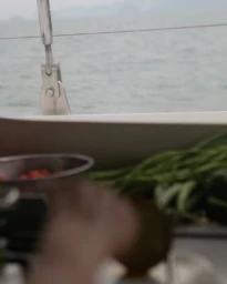Green beans and a bowl of red berries on a boat deck with the ocean in the background