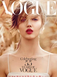 Close-up portrait of a woman with red lips and blonde hair wearing a white spaghetti strap top against an outdoor cornfield background.