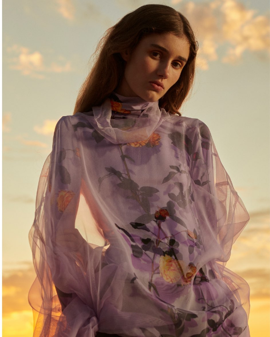 Portrait of a young woman in a floral-patterned, sheer top, against a sunset sky. Fashion, beauty, and portrait photography.
