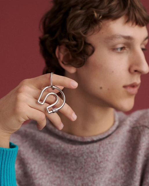 Young adult male holds a silver, horseshoe-shaped object against a red background, wearing a heathered purple sweater and a turquoise sleeve.