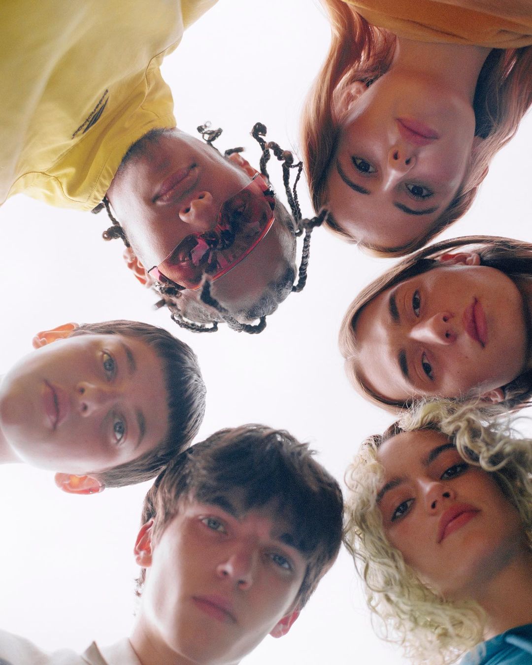 Low angle shot of five young adults looking down at the camera with a bright background, showcasing youth and diversity.