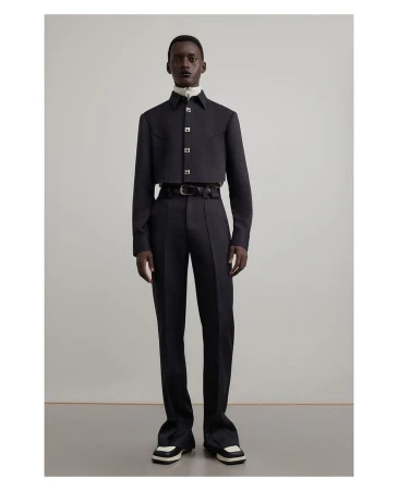 Dark-skinned male model in a black cropped shirt, dress pants, and black-and-white shoes poses in a studio setting.