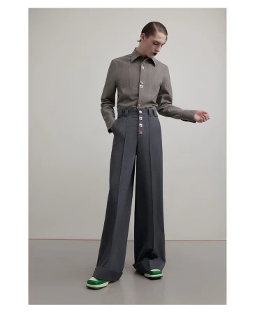 Model in grey buttoned shirt and high-waisted wide-leg trousers standing against a plain studio background.