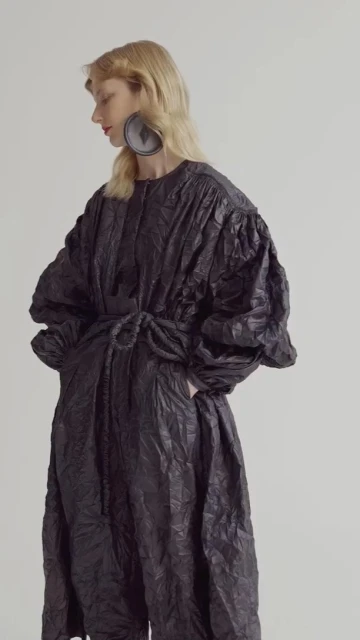 Woman in textured black dress and round earrings poses in a studio, creating an editorial look for fashion design and style concepts.