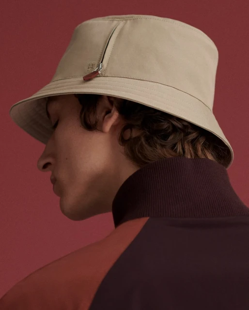 Tan bucket hat on a man with curly dark hair, facing away from the camera, wearing a maroon and rust-colored jacket against a red background.