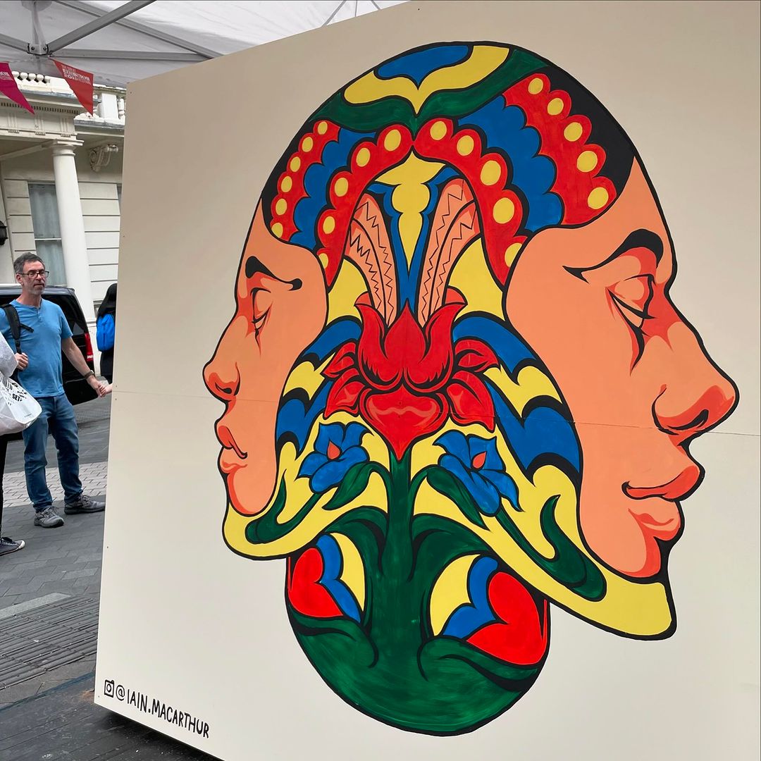 Face art illustration with symmetric faces in profile with closed eyes, stylized lotus design, in reds, blues, yellow, green, cream colors.
