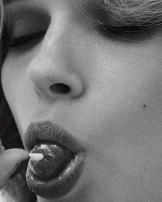 Close-up shot in black and white of an adult female face with eyes closed, and pouty lips with a round candy inside the mouth.