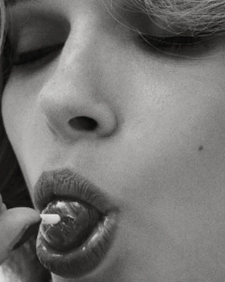 Close-up shot in black and white of an adult female face with eyes closed, and pouty lips with a round candy inside the mouth.