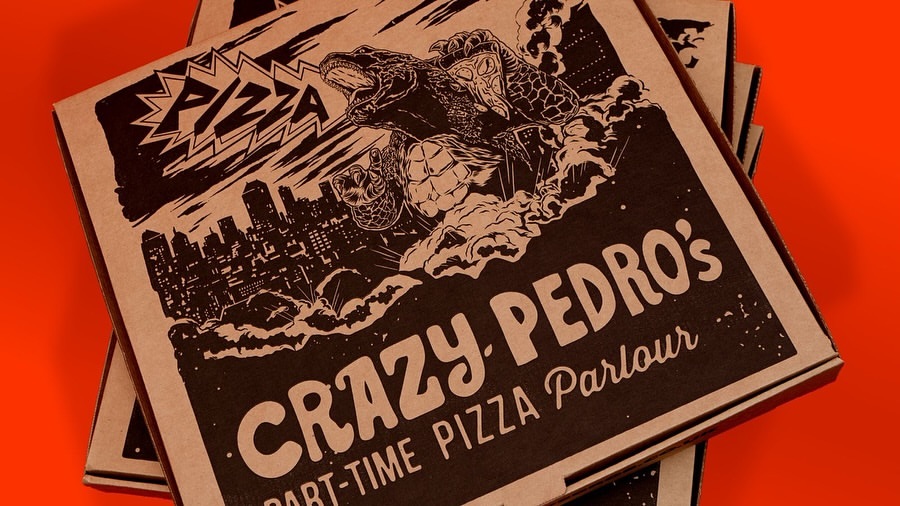 Close-up of stacked pizza boxes with a monster turtle illustration and 'Crazy Pedro's' text, set against a vibrant orange background.