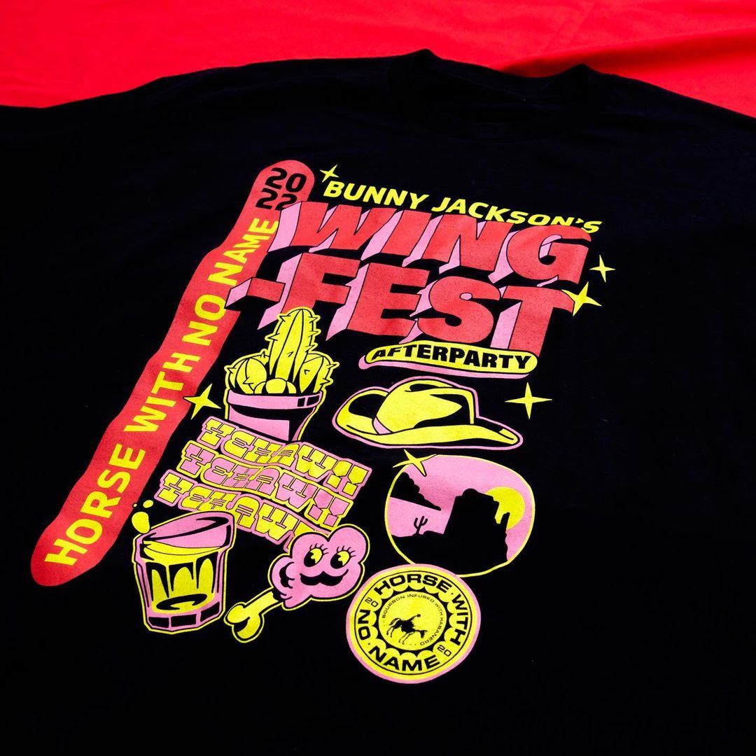 Black t-shirt featuring colorful graphics, including text 'Wing Fest,' cactus, cowboy hat, and desert scene. A fun, vibrant graphic design.