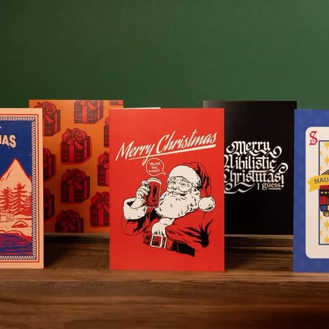 Variety of Christmas cards displayed on a wooden surface, featuring festive and humorous holiday themes and unique designs.