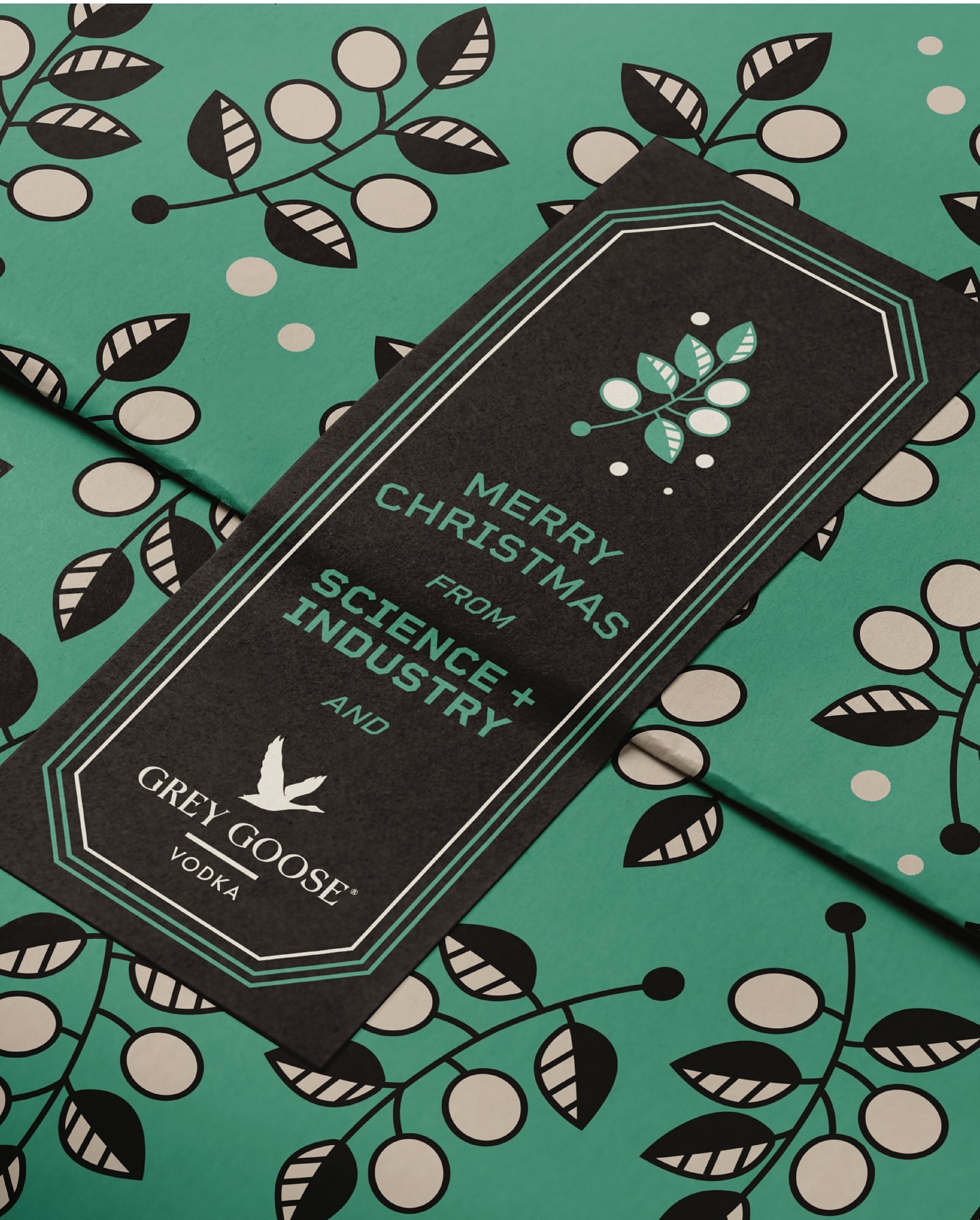 Close-up of a black and green Grey Goose Vodka promotional tag and background. The tag says 'Merry Christmas from Science + Industry'.