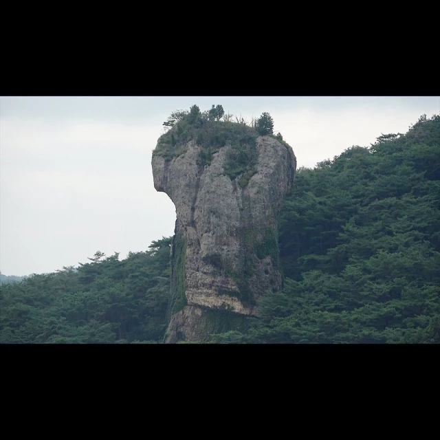 Unique rock formation surrounded by green trees under a cloudy sky, creating a striking natural landscape for travel and exploration.