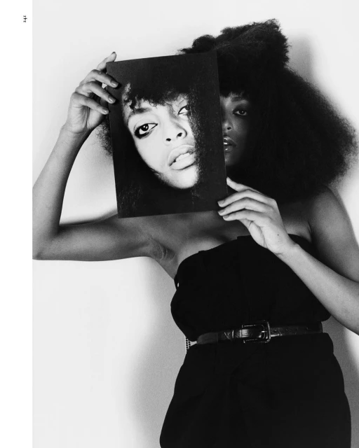 Black and white portrait of a woman holding up a photo of another woman's face, both with dark hair and similar features, in studio.