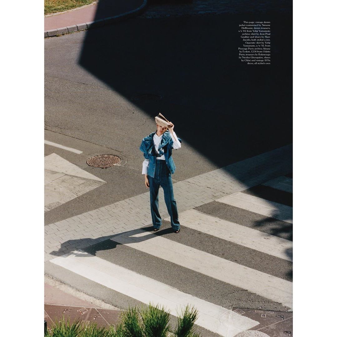 Fashion shot of an adult woman in denim on a pedestrian crosswalk, holding a hat over her face with an asphalt background.