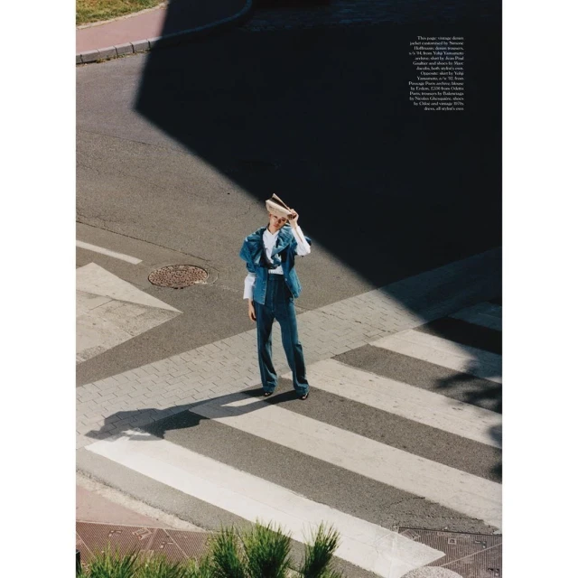 Fashion shot of an adult woman in denim on a pedestrian crosswalk, holding a hat over her face with an asphalt background.