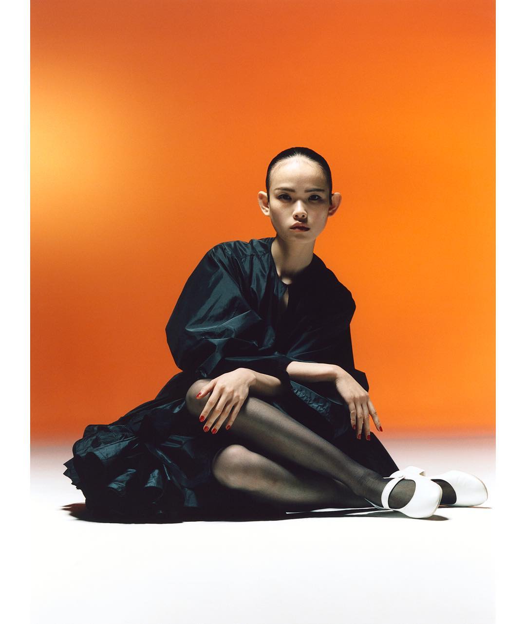 Young adult woman posing in black dress with orange background. Eye-level shot with soft studio lighting. Fashion portrait.
