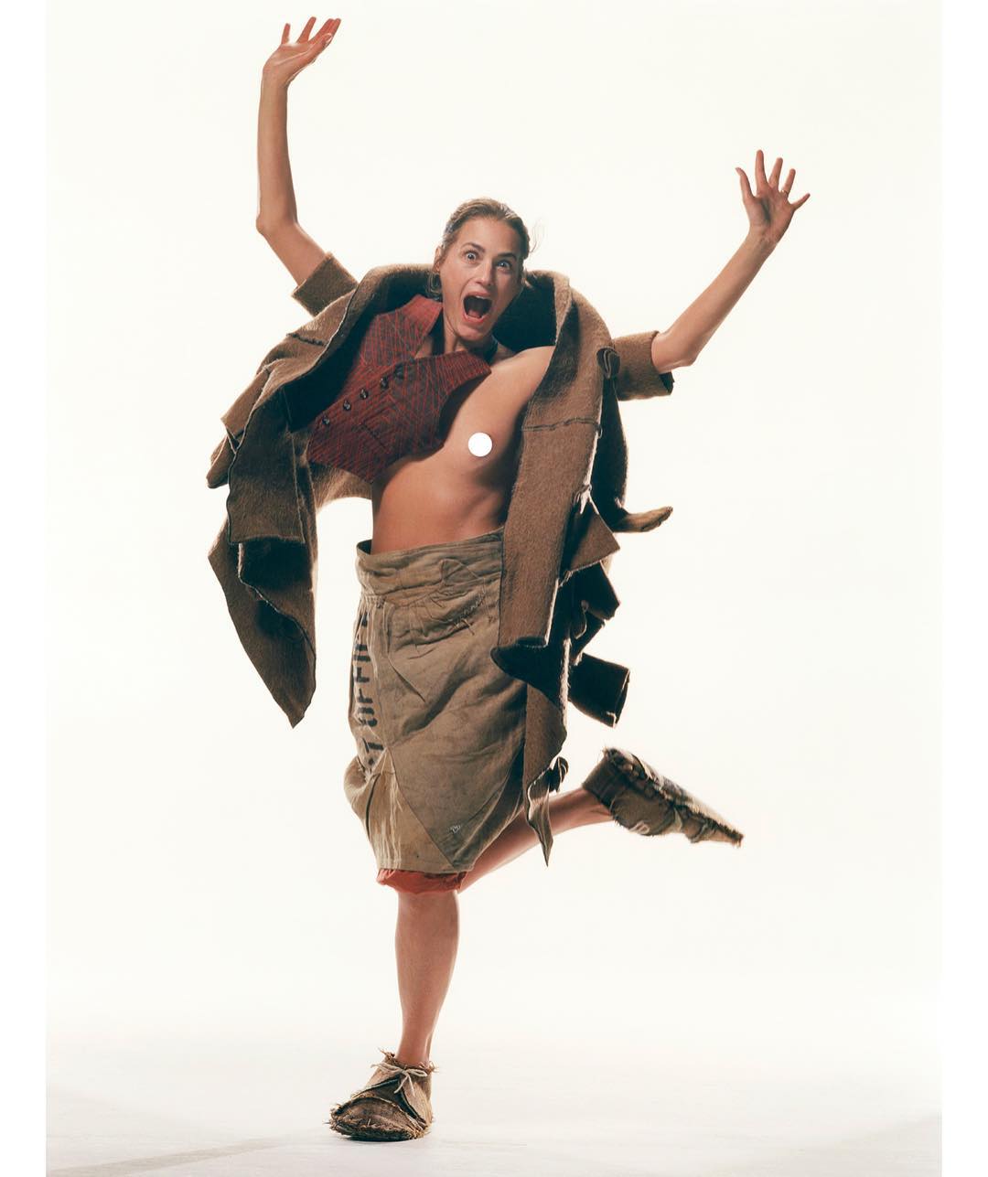 A jubilant adult woman in a deconstructed coat and makeshift skirt strikes a dynamic pose in a photo studio against a white backdrop.