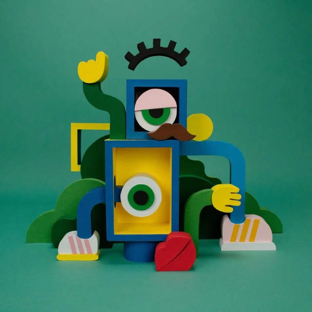 Abstract robot figure assembled from green, blue, and yellow wooden geometric shapes against a solid green background.