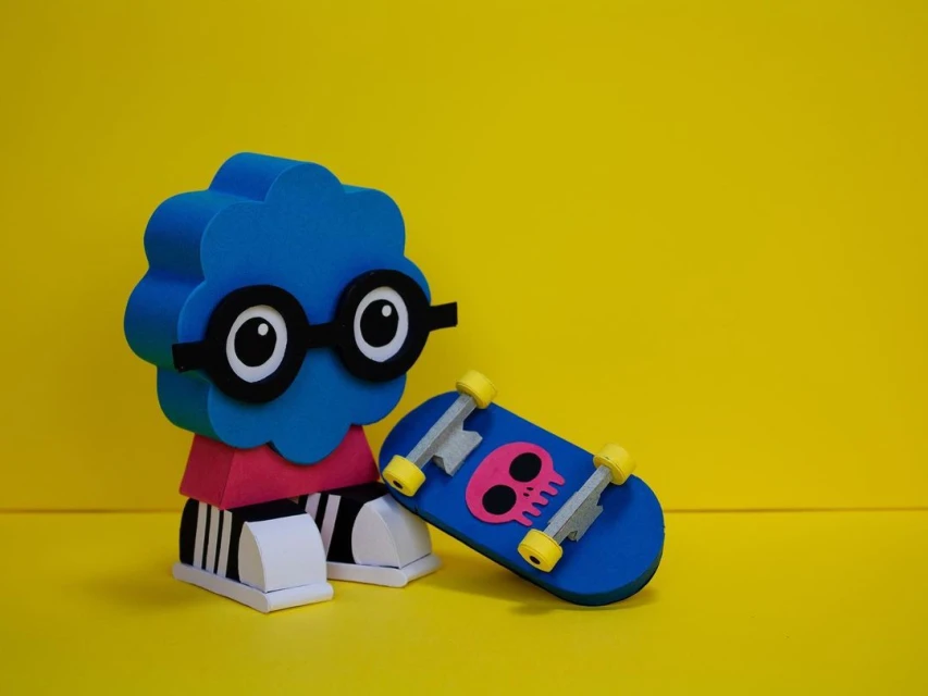Blue cartoon cloud character with glasses sits next to blue toy skateboard with skull, on a bright yellow background.