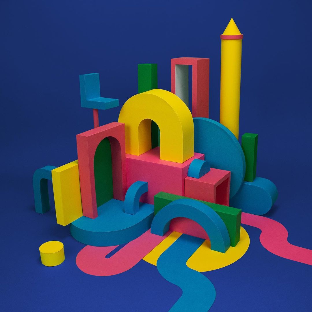 Colorful geometric shapes including arches, cylinders, and cubes arranged in a playful composition against a blue background.