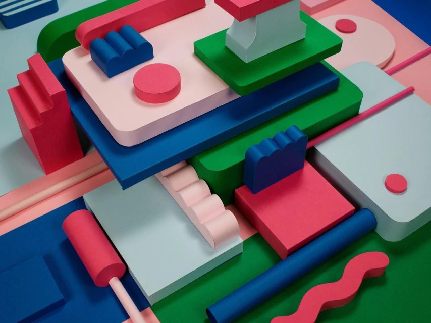 Abstract geometric composition featuring pink, blue, green, and white shapes, cylinders, and blocks in a vibrant, colorful arrangement.