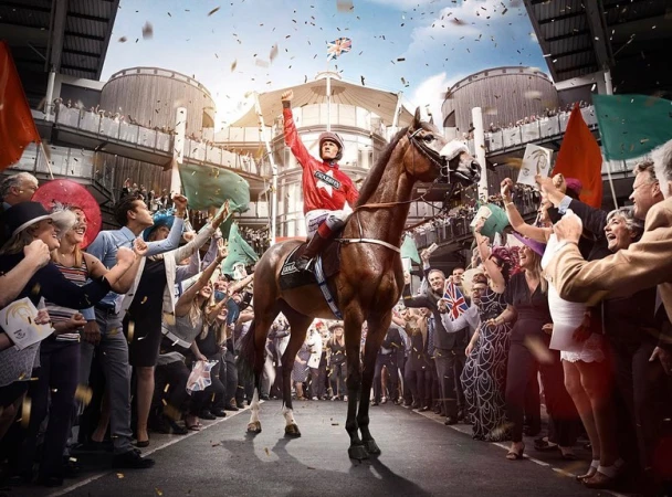 Jockey on horseback celebrates victory with cheering crowd and confetti at daytime horse race event under open stadium roof.