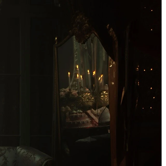 Reflection in ornate mirror showing burning candles on a cake table in a dimly lit, opulent interior with decorative lighting.