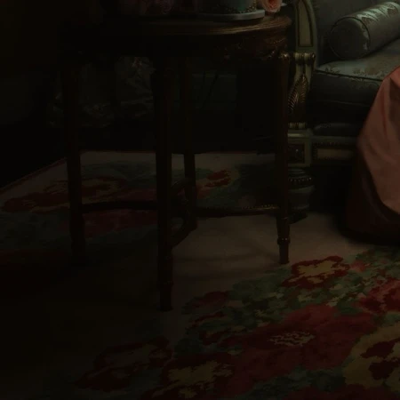 Dark interior scene featuring a vintage floral rug, an ornate table with floral decor, and a partially visible antique chair.
